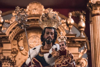A detailed bronze sculpture of King Kosoko in regal attire, set against a deep royal blue backdrop.
