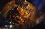 Close-up of a whiskey glass with amber liquid and ice cubes on a wooden table.