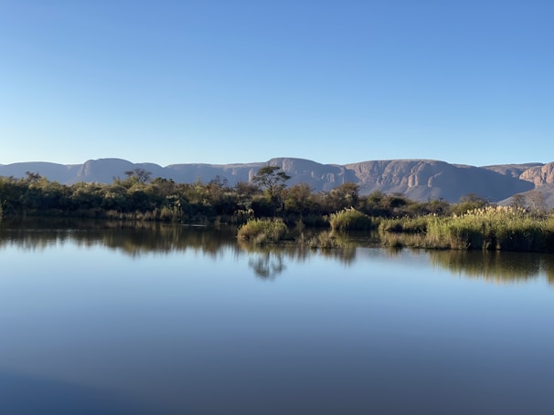 Close-up of a calm lake reflecting the surrounding mountains under a clear sky.