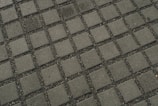 A close-up view of a tiled pavement featuring evenly spaced square concrete tiles separated by small gravel or pebbles, creating a grid pattern.