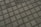 A close-up view of a tiled pavement featuring evenly spaced square concrete tiles separated by small gravel or pebbles, creating a grid pattern.