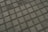 A close-up view of a tiled pavement featuring evenly spaced square concrete tiles separated by small gravel or pebbles, creating a grid pattern.