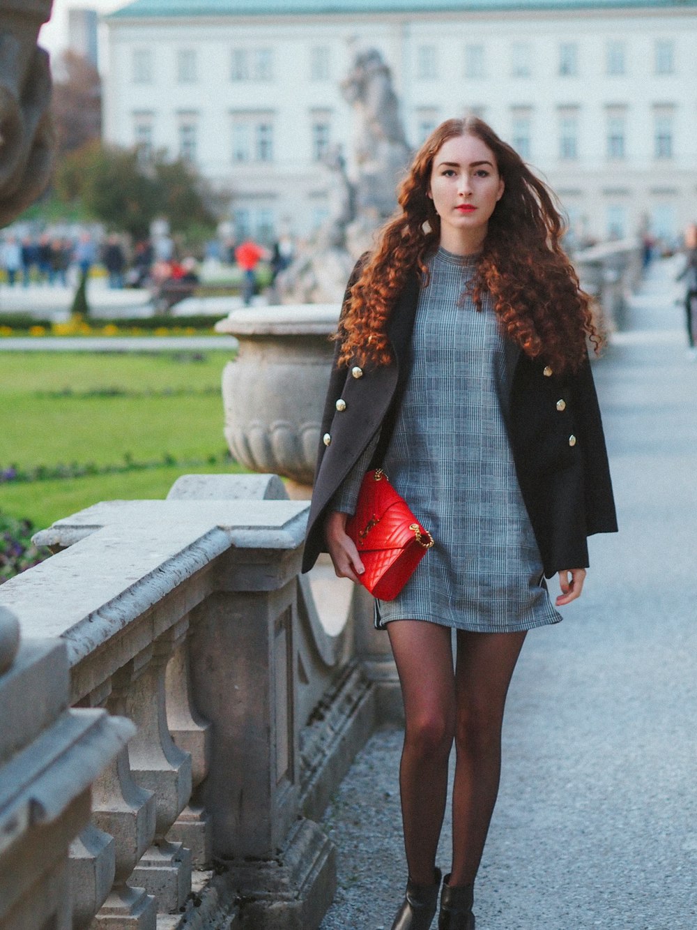 woman in black long sleeve dress and red mini skirt standing on gray concrete bridge during