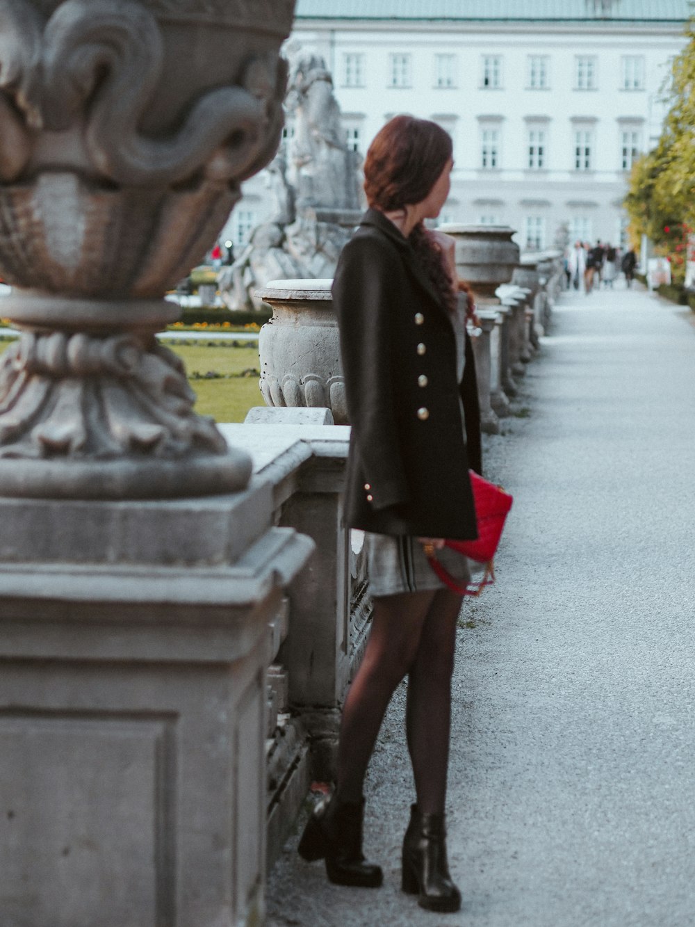 Donna in cappotto nero in piedi sulla strada di cemento grigia durante il giorno