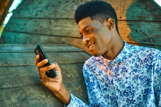 man in blue and white floral button up shirt holding black smartphone