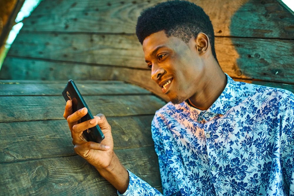 man in blue and white floral button up shirt holding black smartphone