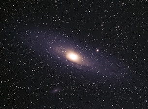 A vast expanse of space filled with numerous stars scattered across the dark sky. At the center, a glowing galaxy with a bright core and spiraling arms is prominent, showcasing the grand scale of the universe.