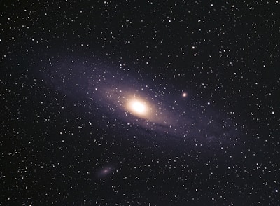 A vast expanse of space filled with numerous stars scattered across the dark sky. At the center, a glowing galaxy with a bright core and spiraling arms is prominent, showcasing the grand scale of the universe.