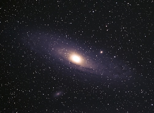 A vast expanse of space filled with numerous stars scattered across the dark sky. At the center, a glowing galaxy with a bright core and spiraling arms is prominent, showcasing the grand scale of the universe.