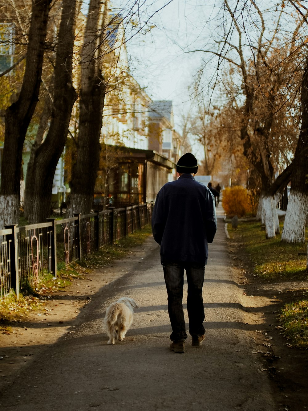 man in black jacket walking on pathway with dog during daytime