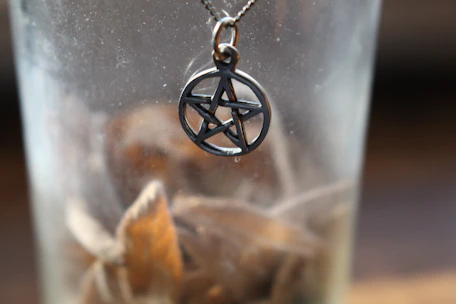 Close-up of hands holding a simple wooden pentacle pendant against mossy bark.