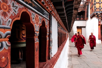 Monks in maroon robes walk past golden prayer bells in a serene Bhutanese monastery setting