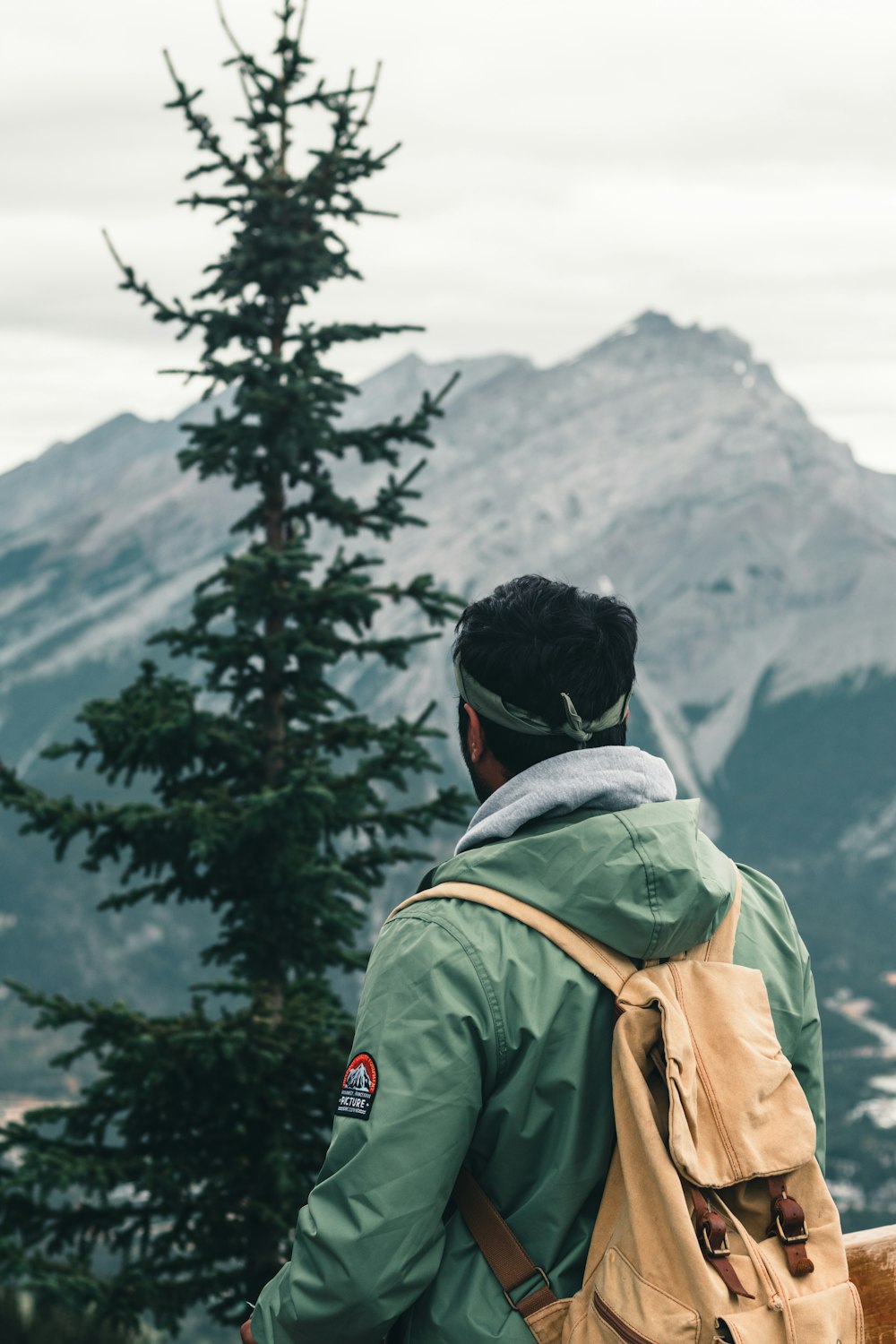 homme en veste verte et sac à dos noir debout près d’arbres verts pendant la journée