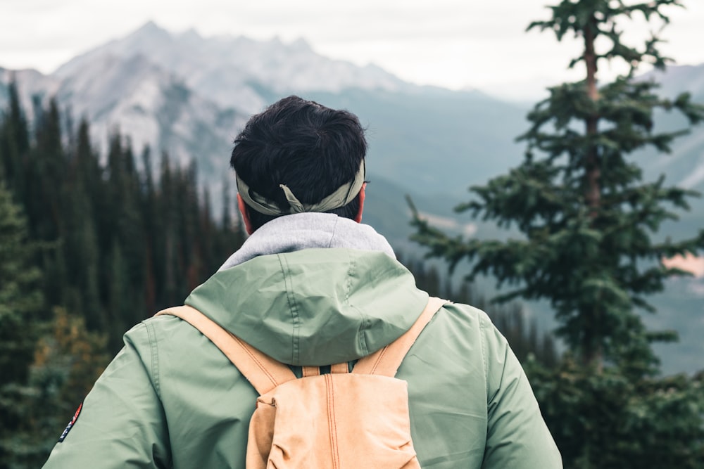 person in green jacket with backpack looking at green trees during daytime