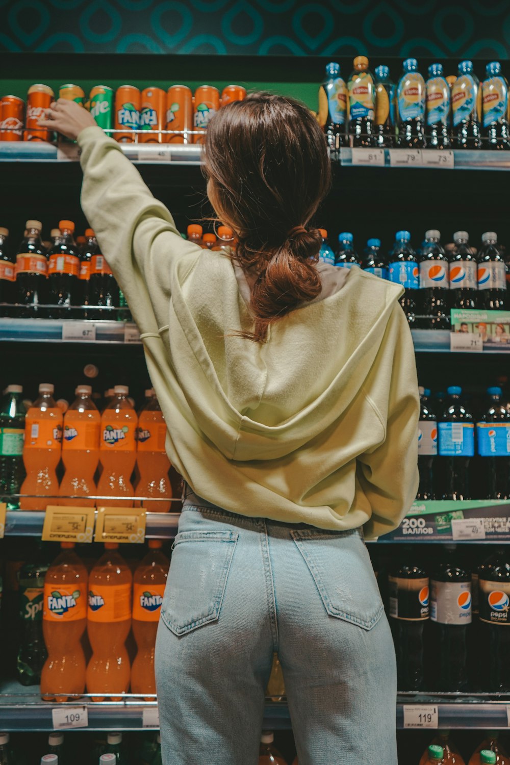 Femme en pull beige et jean bleu debout devant des bouteilles en verre