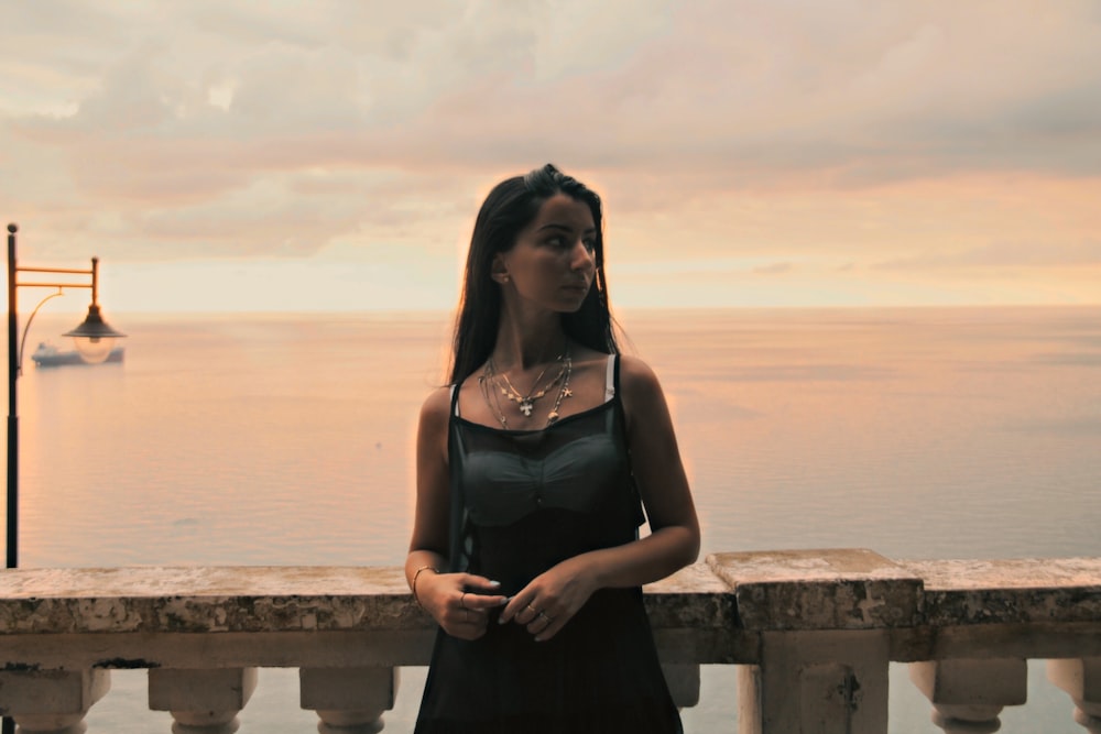 woman in black spaghetti strap dress standing on brown wooden dock during daytime