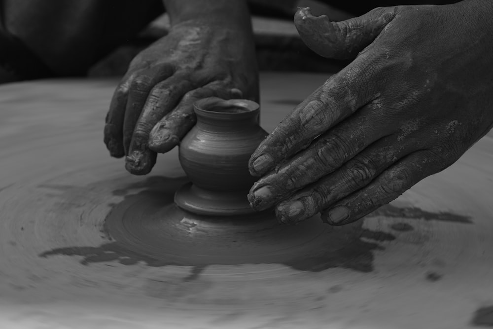 person making clay pot on round wooden seat