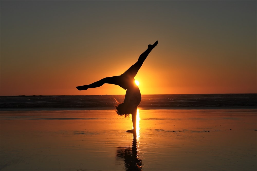 Mujer en vestido blanco de pie en la playa durante la puesta del sol