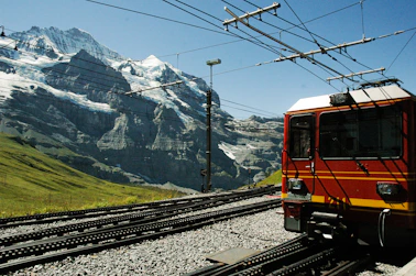 orange and black train on rail tracks near snow covered mountain