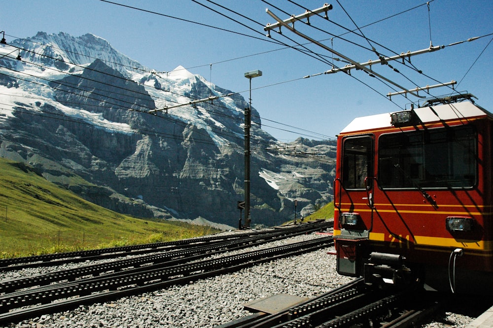 orange and black train on rail tracks near snow covered mountain