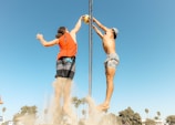 man in orange t-shirt and blue denim shorts holding silver pole during daytime