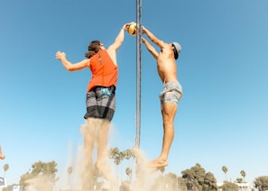 man in orange t-shirt and blue denim shorts holding silver pole during daytime