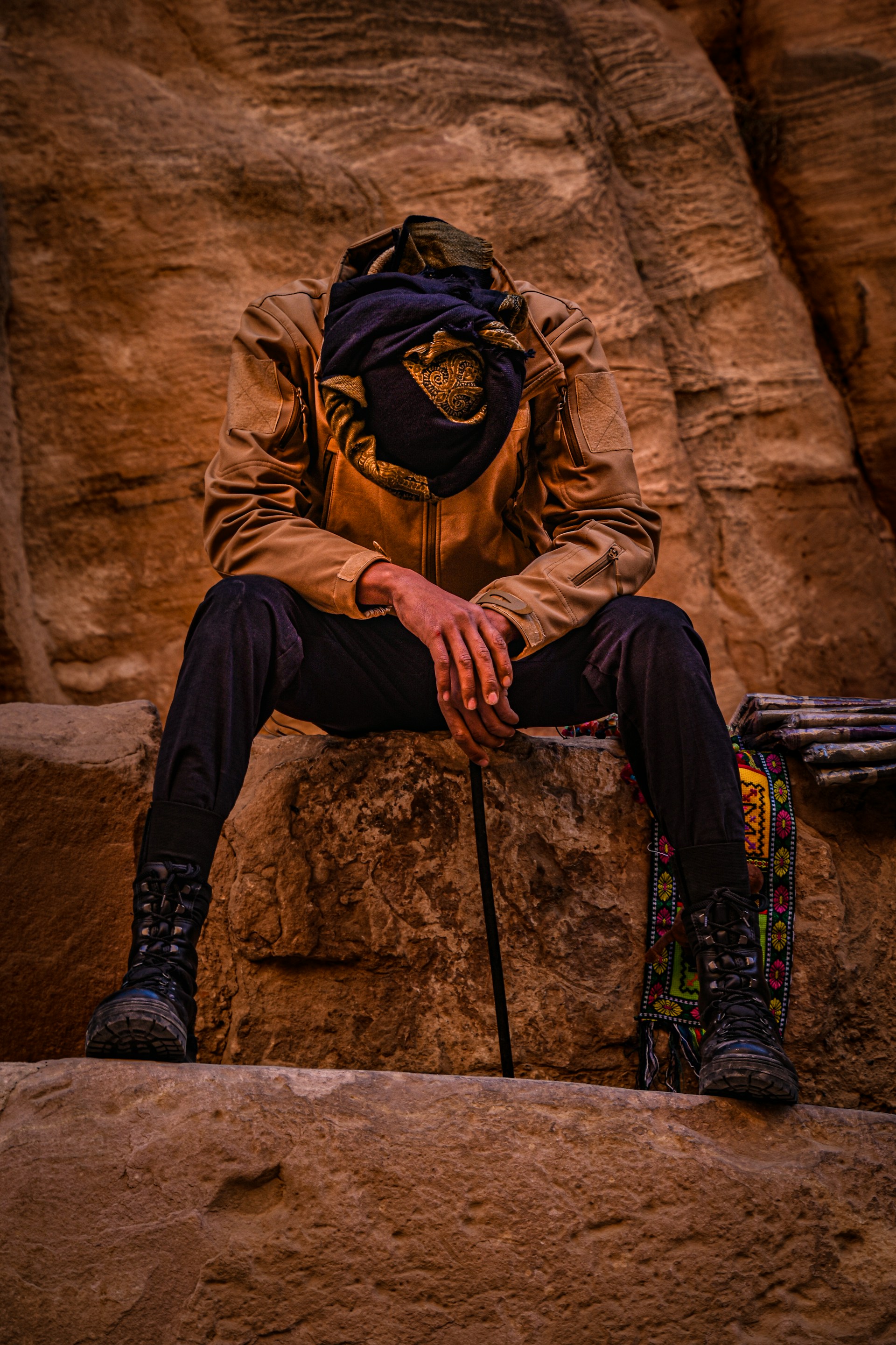 man in brown jacket and black pants sitting on brown rock