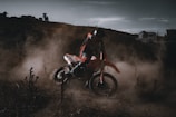 A rider wearing full motocross gear riding through a dusty trail at sunset.