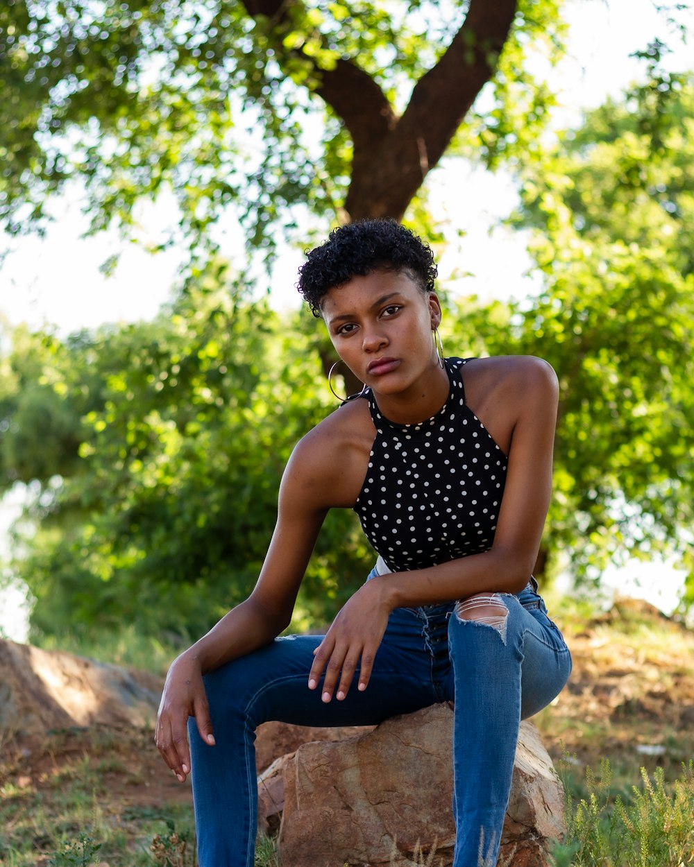 woman in black and white polka dot tank top and blue denim jeans sitting on brown