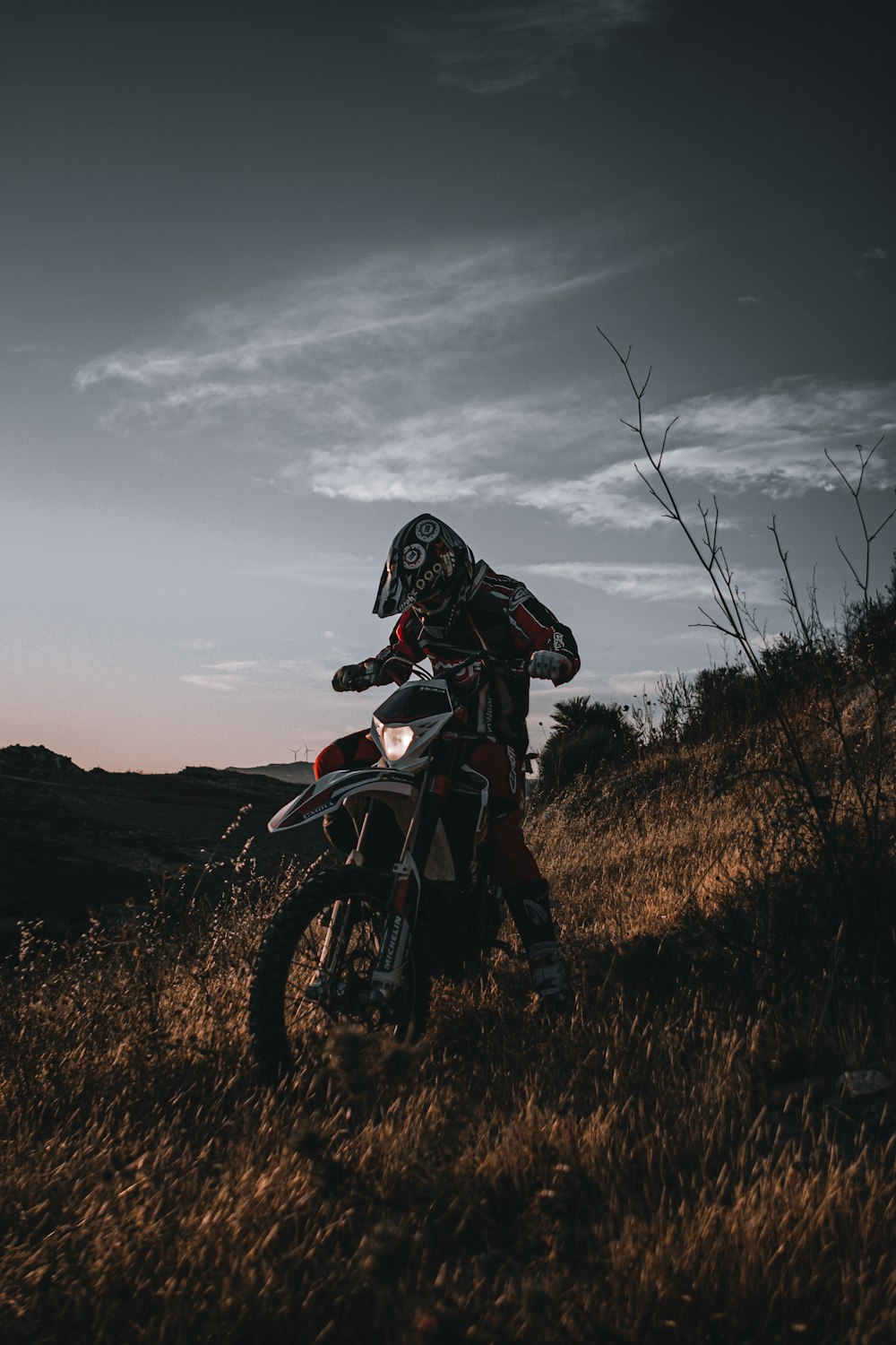 黒と赤のオートバイスーツを着た男が茶色の草原でモトクロスダートバイクに乗っています