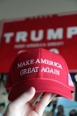 A close-up of a red 'Make America Great Again' style cap resting on a wooden table with soft natural light.