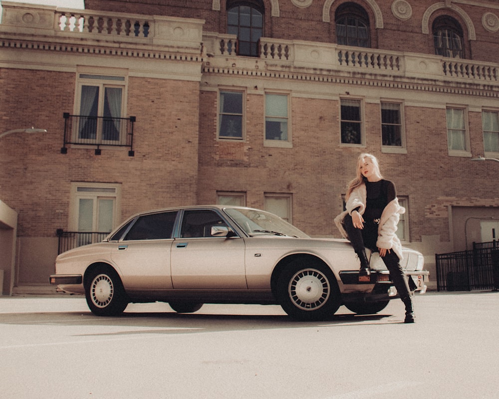 woman in white long sleeve shirt and black pants standing beside silver sedan