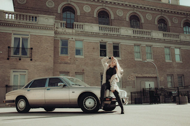 A professional driver standing confidently beside a sleek black car in an urban setting.