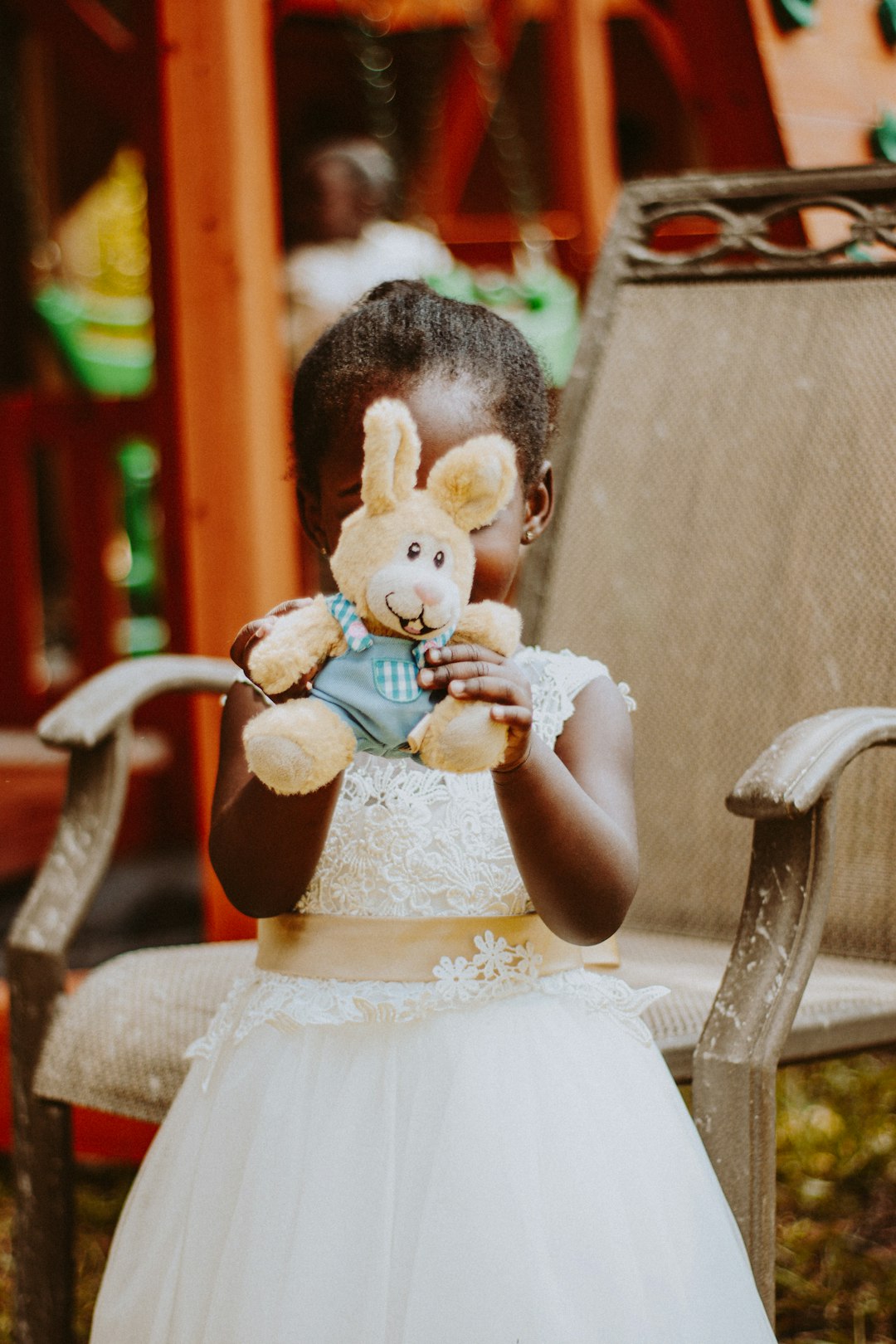 girl in white dress holding white bear plush toy sitting on brown wooden armchair