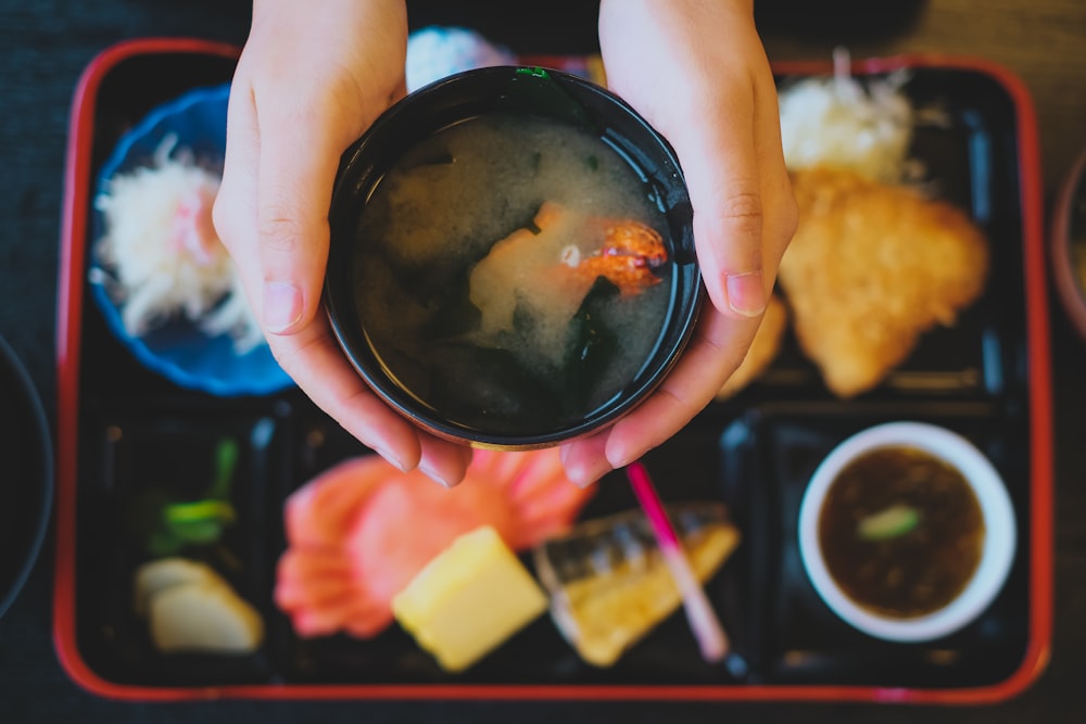 person holding black ceramic bowl with food