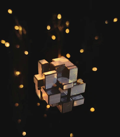 Modern 3D cube sculpture with sharp edges and a matte black finish, illuminated by warm golden lighting.