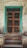 An old wooden door with a turquoise frame stands against a weathered, textured wall. The door features a metal mesh panel and is positioned at the top of a short set of stone steps. The entire scene has a rustic and aged appearance.