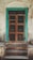 An old wooden door with a turquoise frame stands against a weathered, textured wall. The door features a metal mesh panel and is positioned at the top of a short set of stone steps. The entire scene has a rustic and aged appearance.