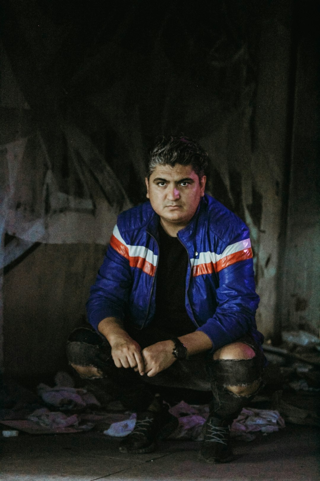 man in blue and red striped long sleeve shirt sitting on black concrete floor