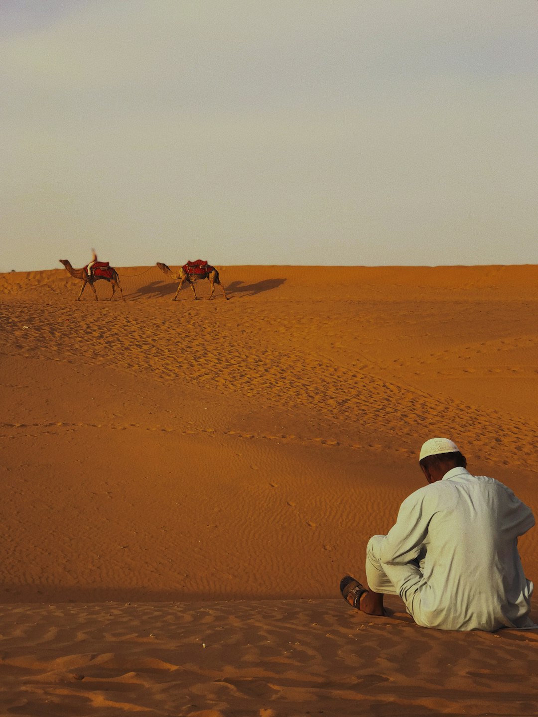 man in white dress shirt riding camel on brown sand during daytime