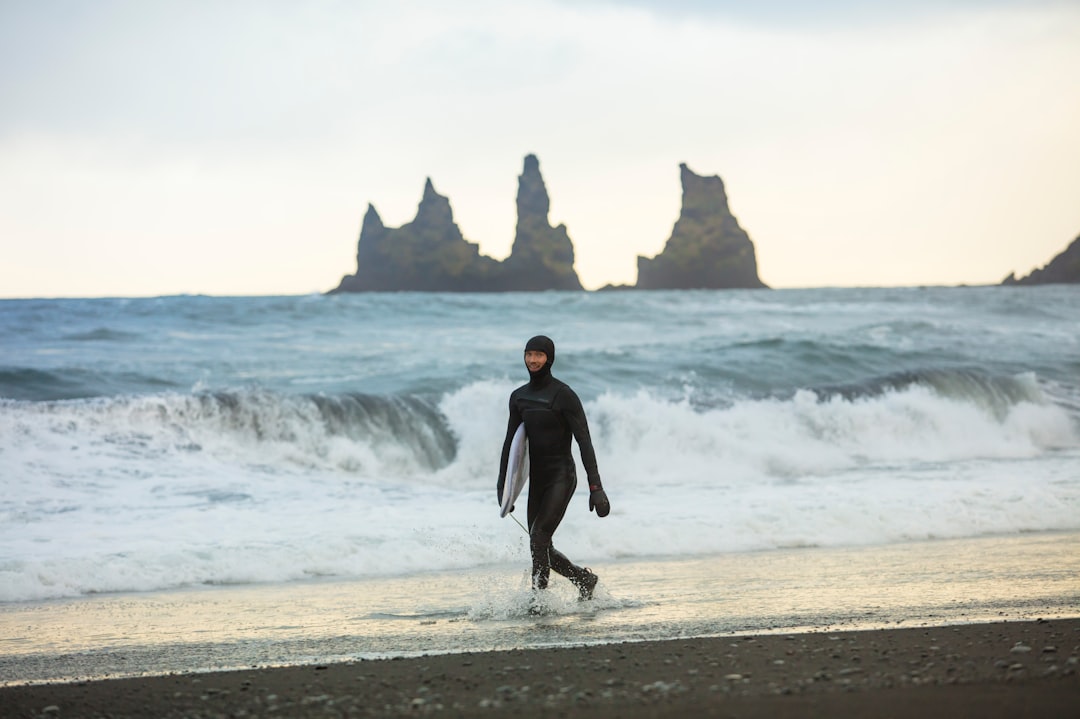 man in black wet suit walking on beach shore during daytime