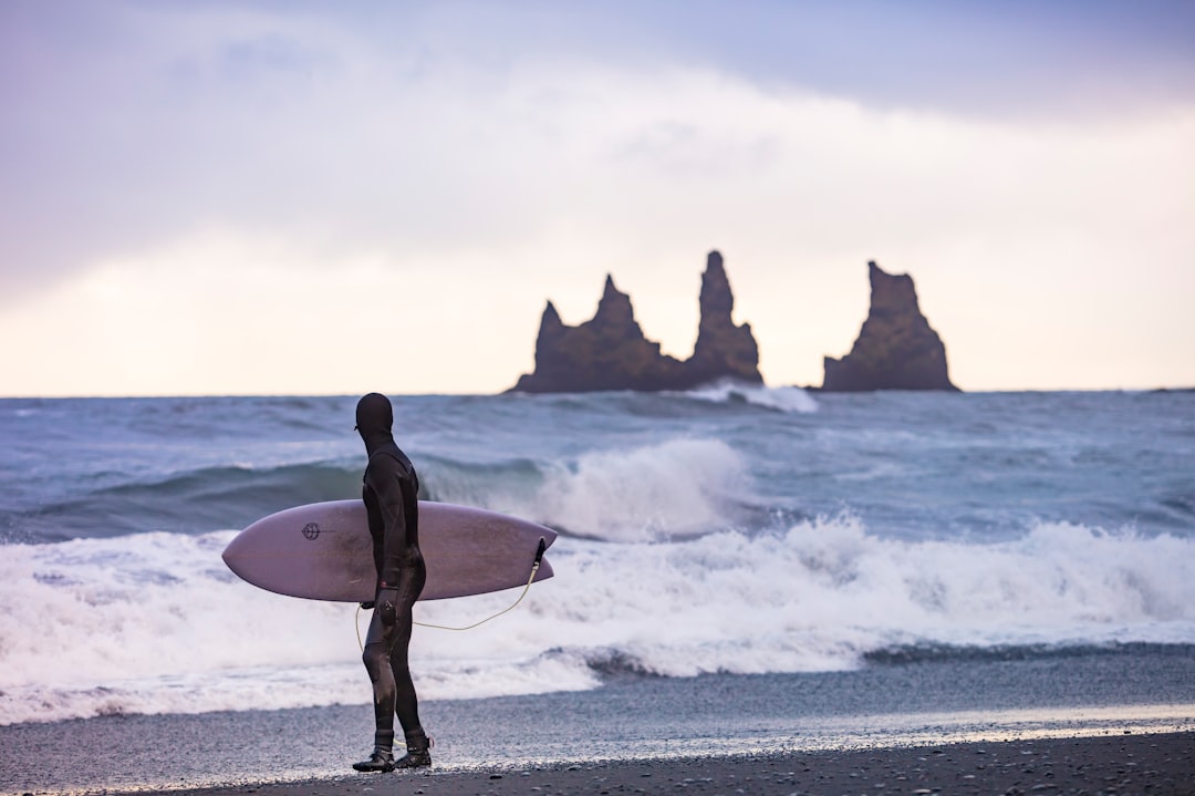 man in black wet suit holding white surfboard walking on seashore during daytime