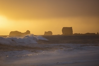 A dramatic shot of crashing ocean waves against rugged cliffs during sunset.