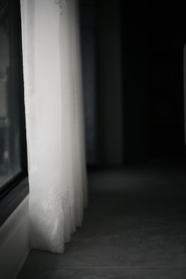 Elegant bedroom featuring light beige sheer curtains flowing beside a large window.