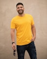 man in yellow crew neck t-shirt and black denim jeans standing beside white wall
