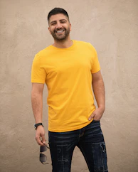 man in yellow crew neck t-shirt and black denim jeans standing beside white wall