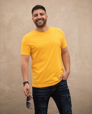 man in yellow crew neck t-shirt and black denim jeans standing beside white wall
