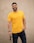 man in yellow crew neck t-shirt and black denim jeans standing beside white wall