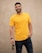 man in yellow crew neck t-shirt and black denim jeans standing beside white wall