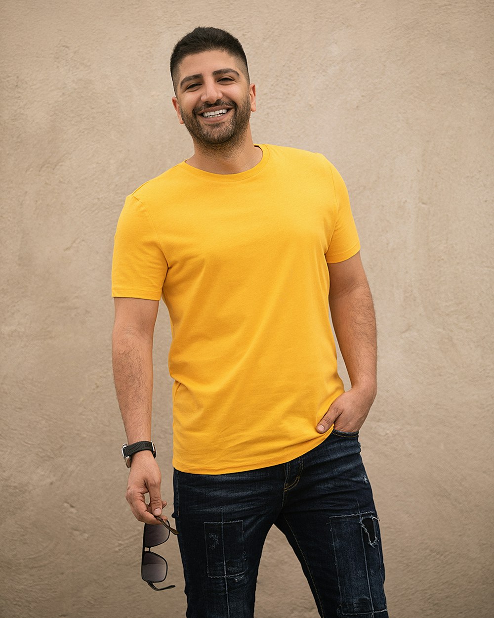 Mann in gelbem Rundhals-T-Shirt und schwarzer Jeans neben weißer Wand